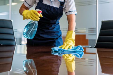 Person reinigt einen Schreibtisch in einem modernen Büro – professionelle Unterhaltsreinigung von SMG